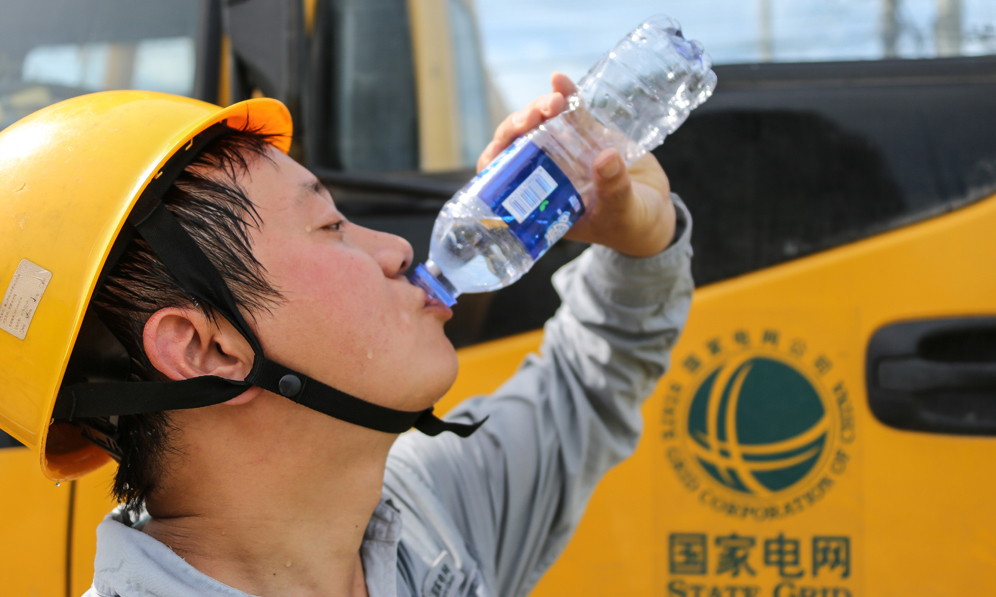 7月19日，安徽黄山供电公司带电作业班的队员们冒着高温，更换线路绝缘子。图为工作结束后，大汗淋漓的供电员工喝水解渴。（黄骏 摄）