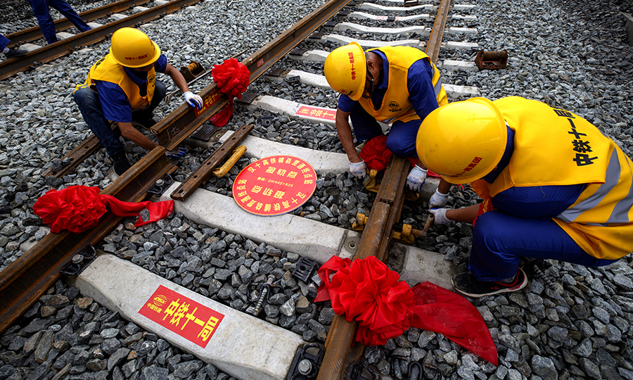 6月22日10时16分，在十堰北站余家山隧道出口，汉十高铁最后一根长钢轨在中国铁建所属中铁十一局三公司WZ500型铺轨机的推送下，精准地落在十堰北站有砟道床的轨枕上，精调之后，轨距误差在正负1毫米之内。在历时8个月铺轨后，我国中西部客运专线的重要组成部分——武汉至十堰高铁实现全线轨道贯通。图为作业人员安装夹板。（彭特 摄）