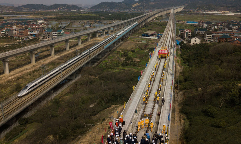 3月12日，中铁四局施工技术人员在传芳特大桥上进行杭黄铁路的铺轨作业，一列高铁从旁边的沪昆客运专线上驶过（无人机拍摄）。（新华社记者 黄宗治 摄）