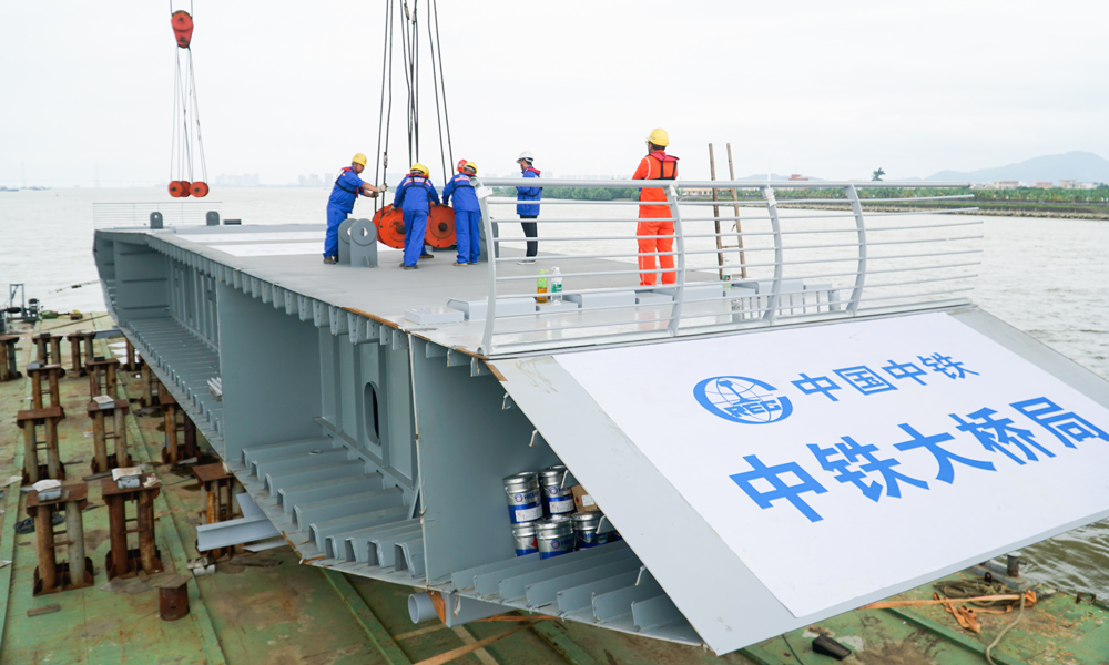 面对地质条件复杂、大型设备及临时设施抗风要求高、风险大，高温洪水恶劣天气等诸多难题，项目部大力引进机械设备，改革创新施工工艺。为了不影响通航，项目团队在施工设计中，将4号主栈桥创新性设计为可提升式钢栈桥。在塔柱施工中，项目团队研发了变截面斜塔钢筋骨架整节段分块预制安装建造技术，将大量高空作业转化为地面作业，减少人员高空作业量达60%以上。采用“步履顶推”塔梁同步施工工艺，在主塔施工的同时架设边跨钢箱梁，有效节约工期约3个月。图为近日拍摄的南中高速洪奇门特大桥施工现场。