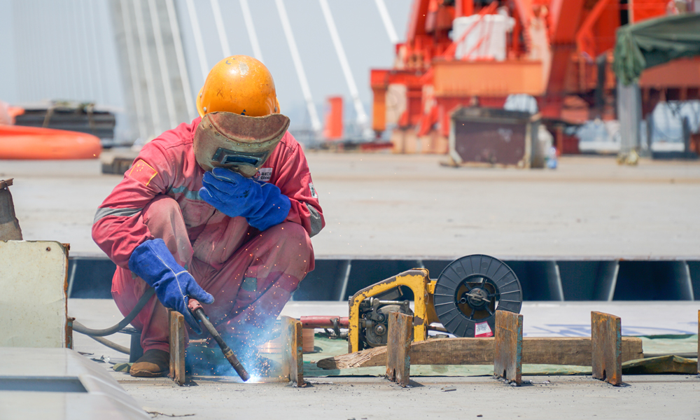 中铁工业历时一年半，完成了大桥2.8万吨共75个钢箱梁制造任务。项目团队建立了全类型梁体三维立体模型，并在此基础上建立全桥焊缝地图，配合云平台智能焊接管理系统，实时记录并保存现场施工焊接参数、环境指标等数据，使梁段主要焊缝监控覆盖率、追踪率均达到100%，全面提升了钢桁梁制造自动化、数字化、网络化、智能化制造水平。图为5月21日，工人在南中高速洪奇门特大桥进行施工作业。