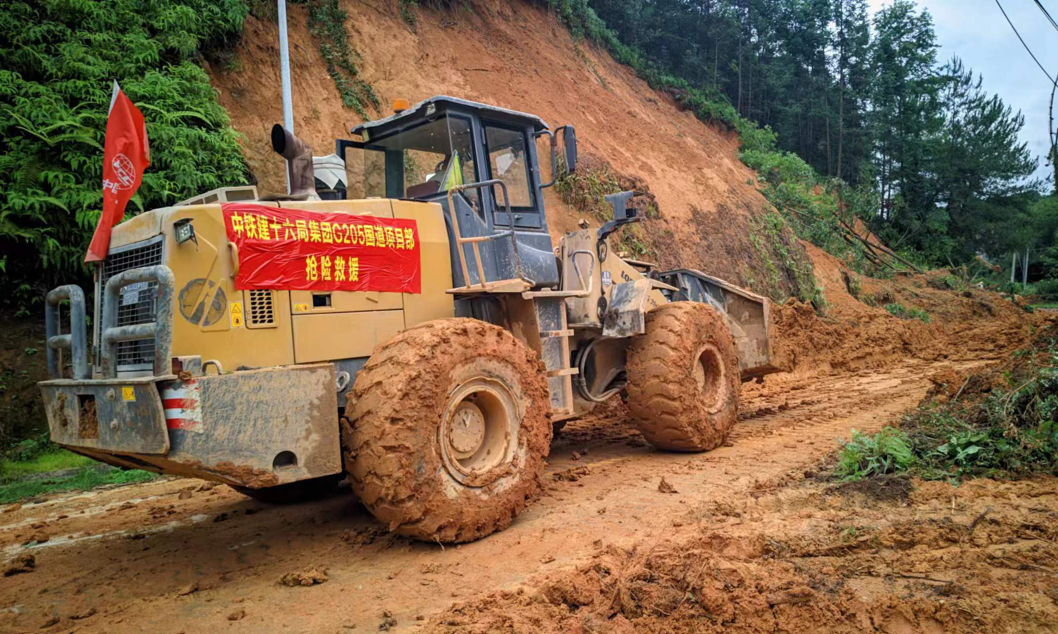 受持续强降雨影响，连日来，福建省龙岩市武平县多处乡镇出现不同程度的山体滑坡、洪涝灾害等情况。6月17日，中铁十六局国道G205项目紧急组织16名人员成立抗洪抢险突击队，调集8台大型机械设备奔赴所在地武平县十方镇、中赤镇及下坝乡重点受灾区，先后疏通生命通道23公里，完成决堤河道整治205米，救助受困人员23名、护送中考考生25名，全力挽回群众财产损失，为当地应急抢险救灾工作提供了强力保障。图为救援人员驾驶推土机疏通乡道。