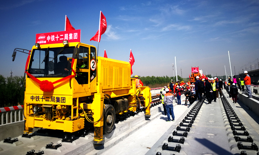 4月15日上午9时28分，在北京至雄安新区城际铁路李营段施工现场，中国铁建所属中铁十二局集团现场指挥人员一声令下，第一组500米长钢轨从T11运输车前端缓缓送出，标志着京雄城际铁路建设整体从线下施工转入线上轨道铺设阶段，也意味着京雄城际铁路（北京段）开通运营进入最后冲刺阶段。图为牵引长轨。